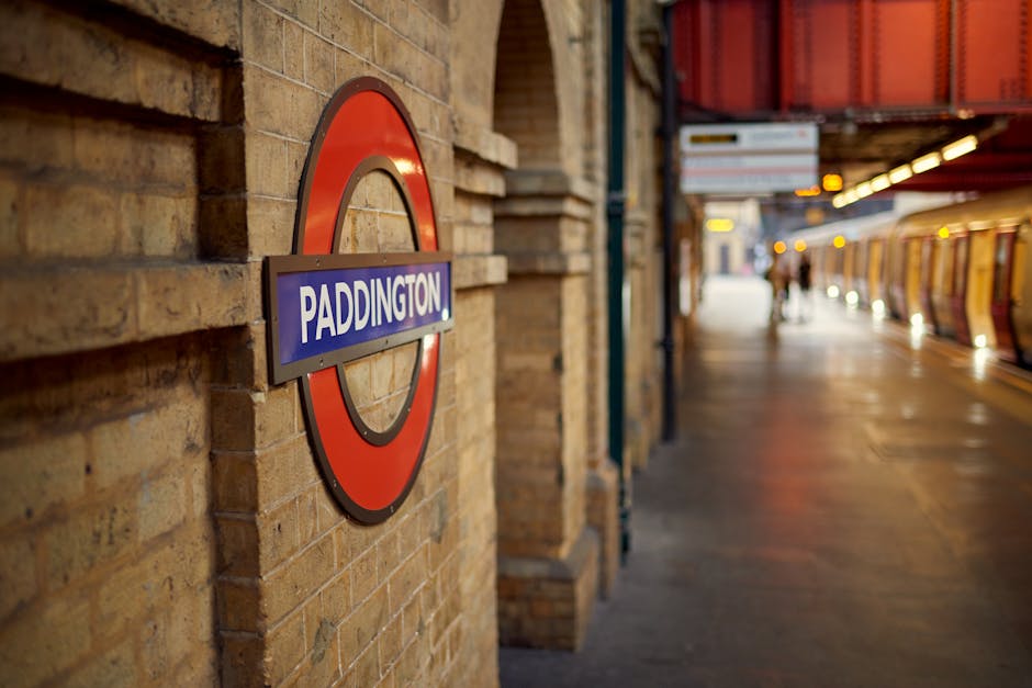 An empty underground tube station platform with a curved, beige concrete ceiling and tiled floor. On the right side, there is a long white wall decorated with large advertisements and posters, some fe